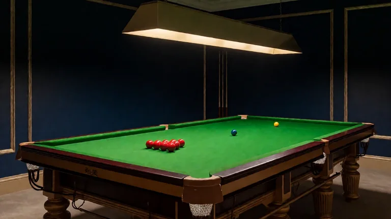 ညအချိန် snooker ကစားခန်းတွင် မီးအိမ်ရှည်အောက်ရှိ အစိမ်းရောင် snooker စားပွဲ၊ တြိဂံပုံ စီထားသော Red ဘောလုံးများနှင့် နေရာအသီးသီးရှိ အရောင်ဘောလုံးများ ပါသော အယူအဆပုံ